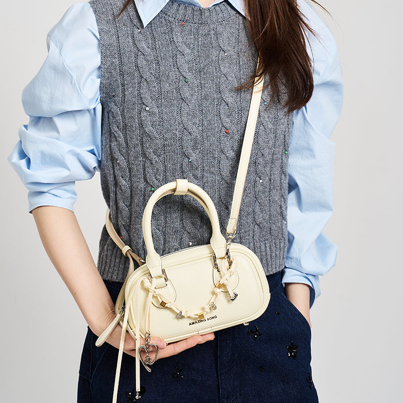 Woman in grey knit vest holding Amazing Song cream handbag crossbody, fashion style