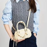 Woman in grey knit vest holding Amazing Song cream handbag crossbody, fashion style