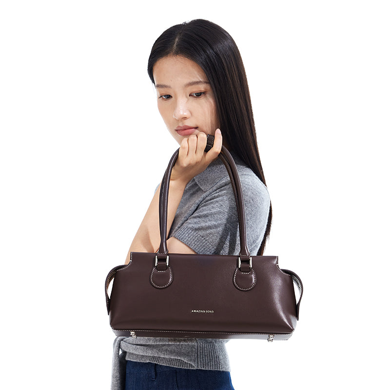 Woman holding brown Amazing Song handbag against white background