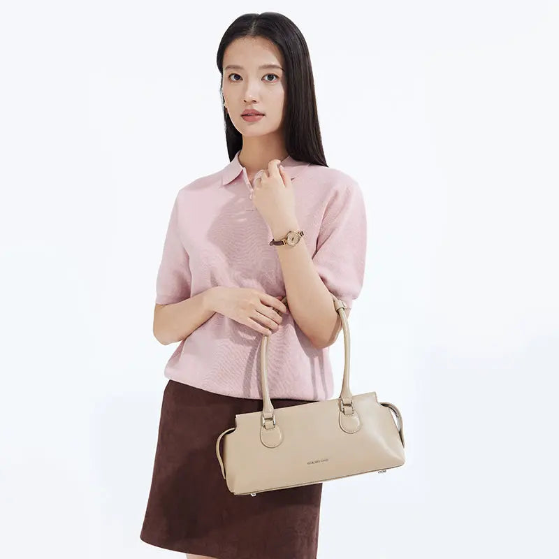 Woman in pink top and brown skirt holding beige Amazing Song handbag against white background