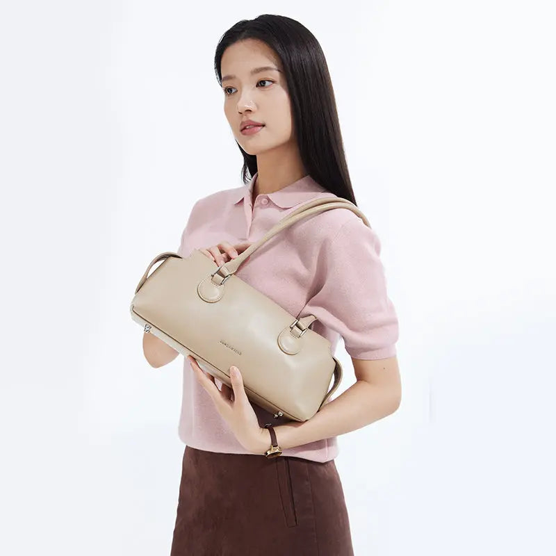 Woman in pink top holding beige Amazing Song handbag, minimalist background