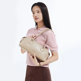 Woman in pink top holding beige Amazing Song handbag, minimalist background