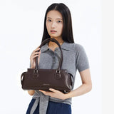 Woman holding brown leather Amazing Song handbag, grey polo sweater, minimal backdrop