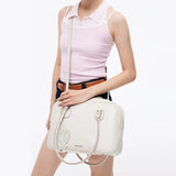 Woman in light pink top holding white Amazing Song handbag with heart charm