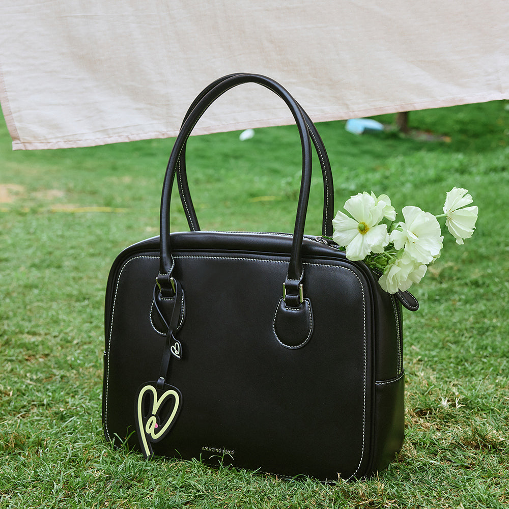 Amazing Song black handbag with heart charm and white flowers on grass outdoors