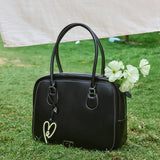 Amazing Song black handbag with heart charm and white flowers on grass outdoors
