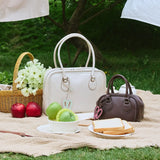 Picnic scene with white and brown handbags, apples, bread, basket of flowers on grass, Amazing Song