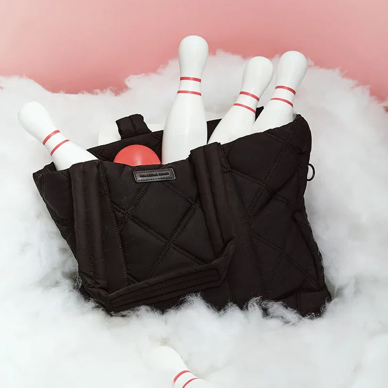 Black quilted Amazing Song bag with bowling pins and red ball on white fluffy surface