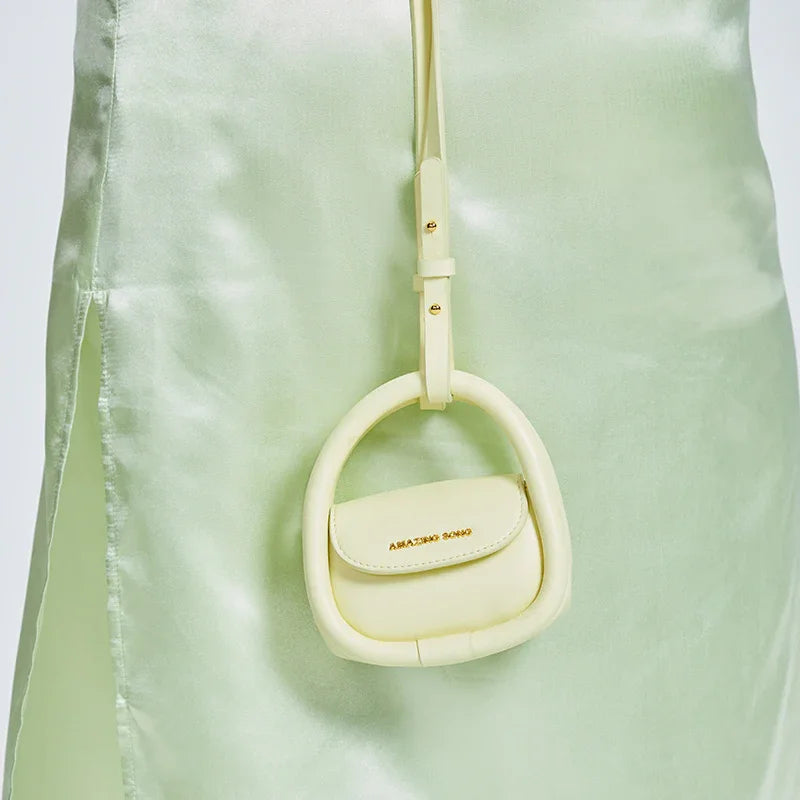 Pastel yellow mini handbag with Amazing Song logo, hanging on a light green satin dress