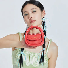 Model in light green dress holding red Amazing Song mini handbag, braided hair, white background