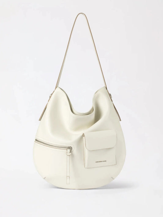 The soft slouchy Liqueur hobo bag in warm cognac leather draped over a shoulder in natural daylight