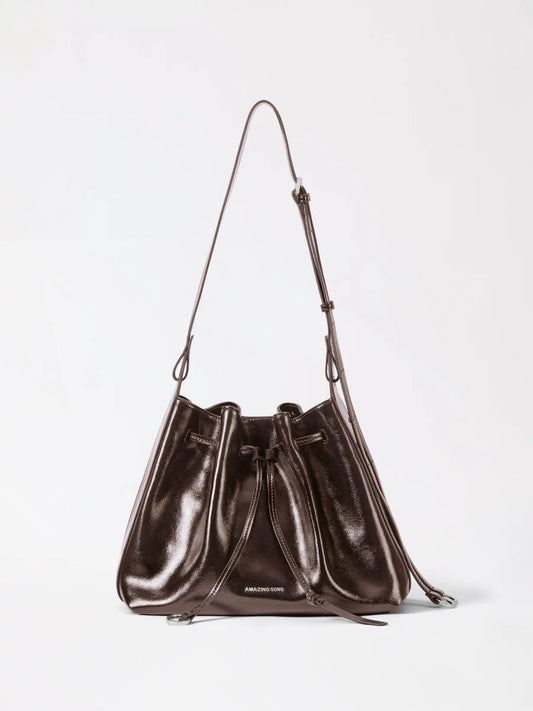 A cute bucket bag in tan leather with a drawstring top and a rounded base sitting on a plain surface