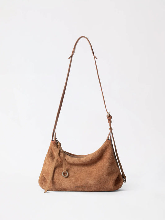 Large suede donut hobo bag in tan resting on a bar counter beside a phone and lipstick
