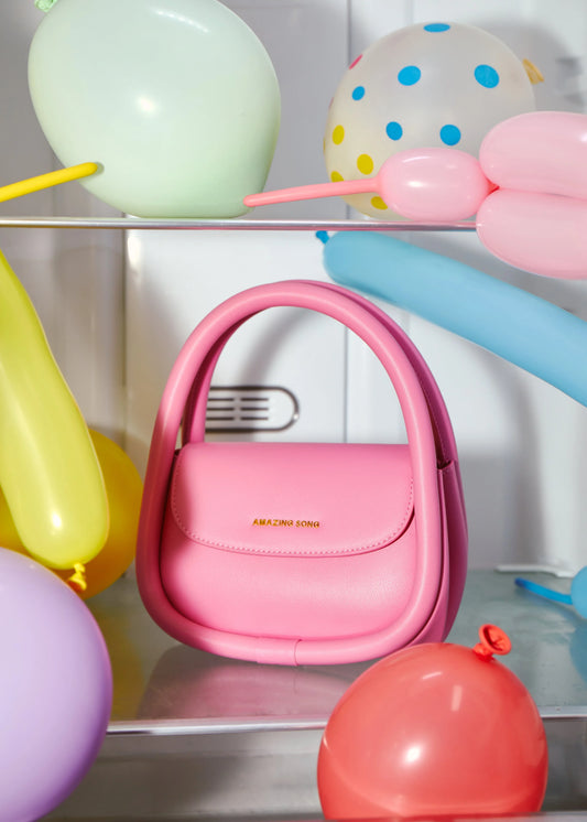 Pink Amazing Song handbag surrounded by colorful balloons on a shelf