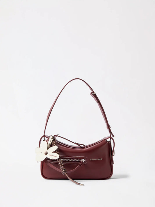 A small mahjong-tile shaped leather bag in warm tan resting on a knit throw