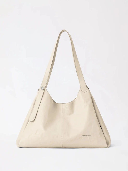 A berry-coloured top-grain leather tote bag standing upright on a pale stone surface in warm light
