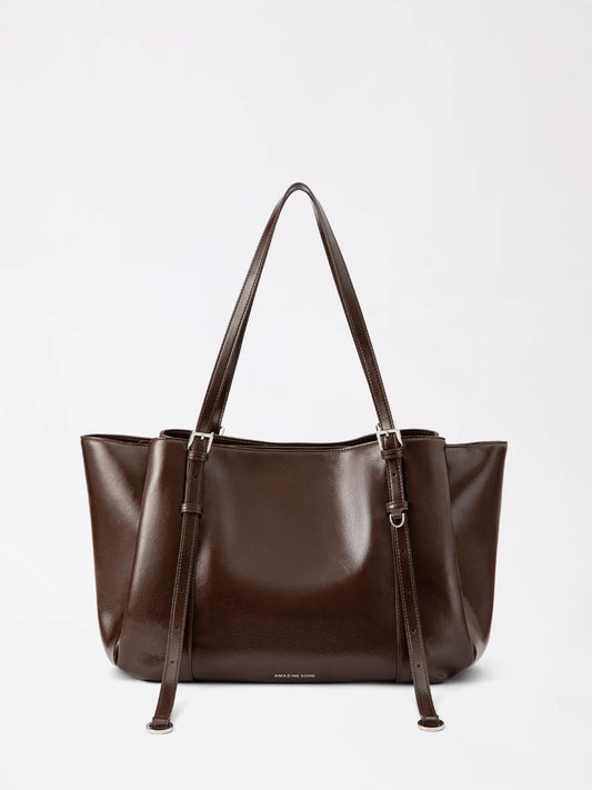 A soft donut-shaped leather tote bag in warm tan on a wooden chair