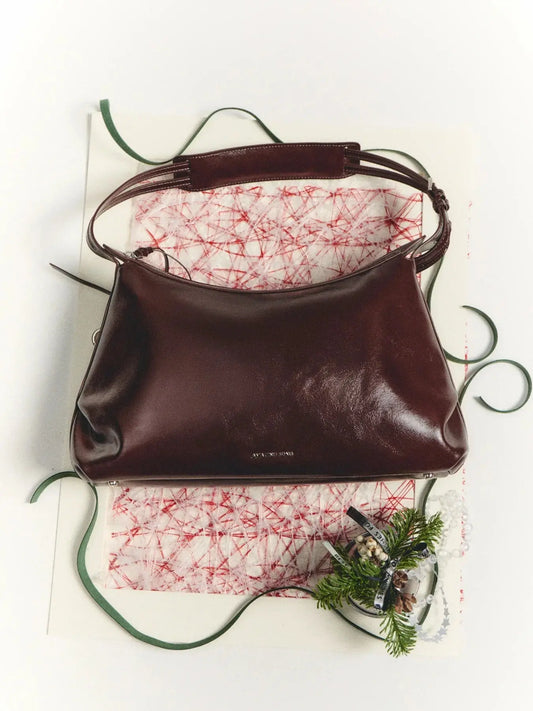 Burgundy leather Amazing Song handbag on festive paper with green ribbon and holiday decor.