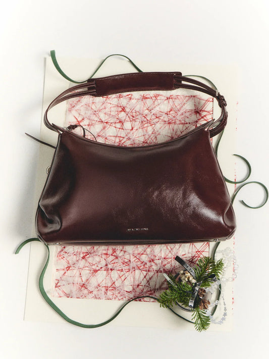 Burgundy leather Amazing Song handbag on festive paper with green ribbon and holiday decor.