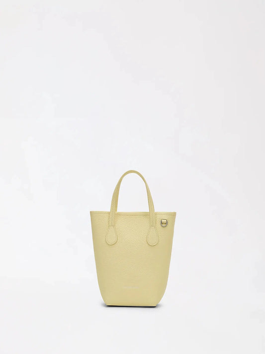 A top-grain leather travel bucket bag in warm tan worn crossbody beside a carry-on suitcase