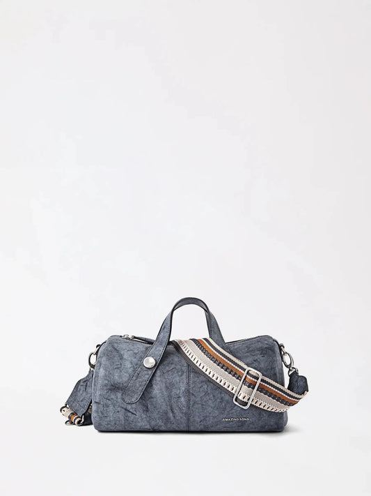 A compact berry-shaped top-grain leather crossbody bag in deep red held by a woman in a cream winter coat