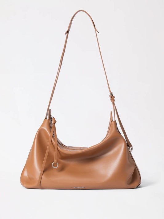 A slouchy donut-inspired leather hobo bag in warm tan resting on a linen surface