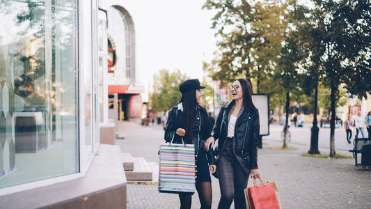 Two women walk down a street with shopping bags.