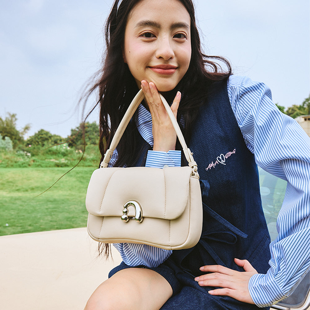 Woman outdoors smiling and displaying a beige handbag, Amazing Song fashion accessory