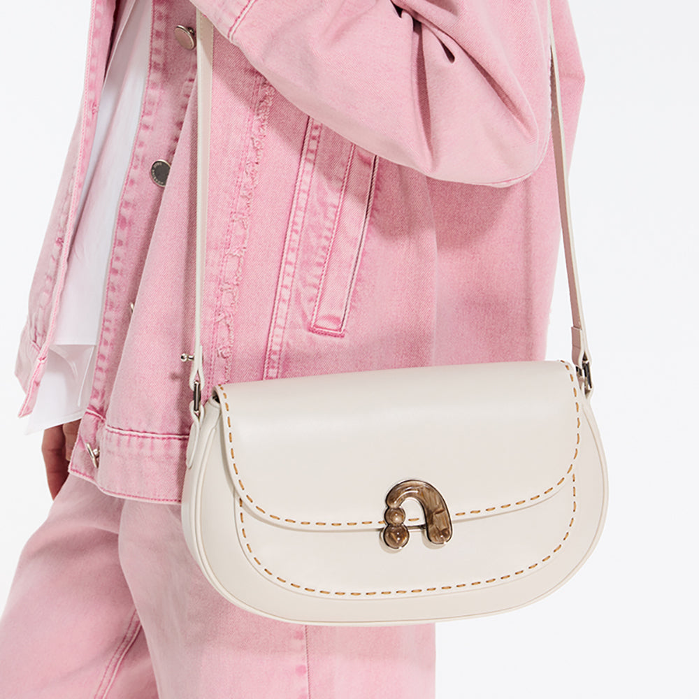 Cream leather crossbody bag with gold clasp, worn over a pink denim jacket and pants