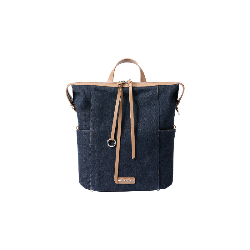 Dark blue denim tote backpack with tan leather straps, Amazing Song logo on front, white background