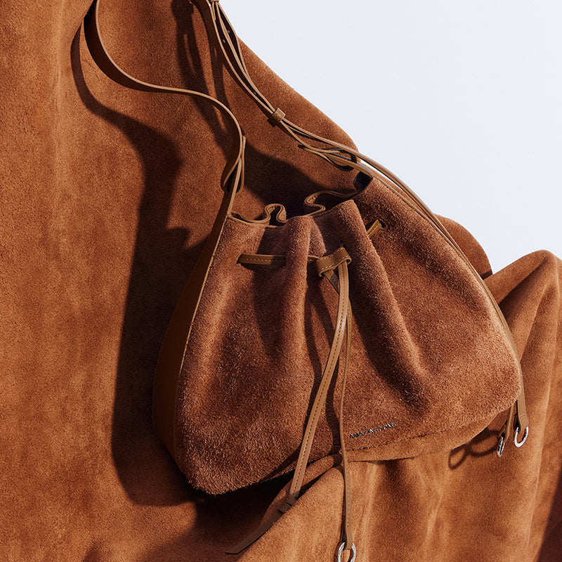 Brown suede bucket bag with leather straps on matching suede background, Amazing Song
