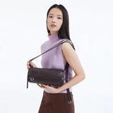 Woman with long hair in a lilac sleeveless turtleneck holding a brown shoulder bag