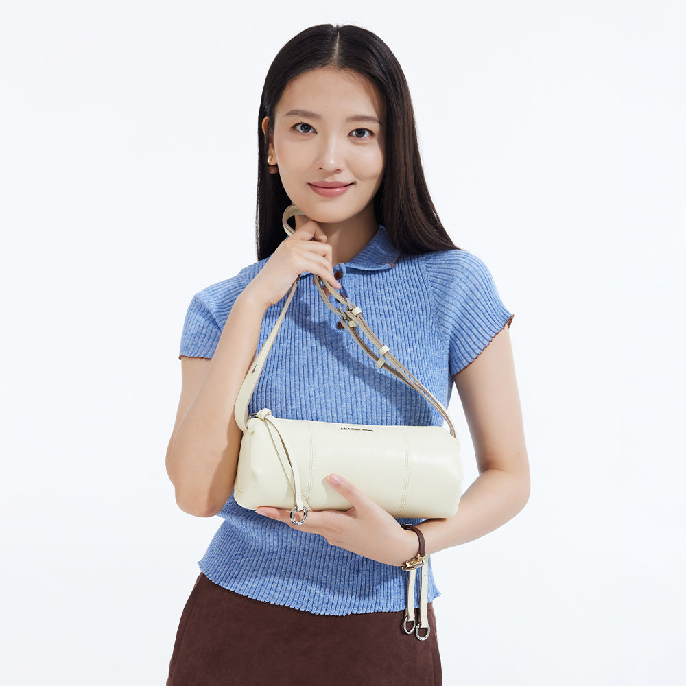 Woman in blue ribbed top holding cream Amazing Song handbag on white background