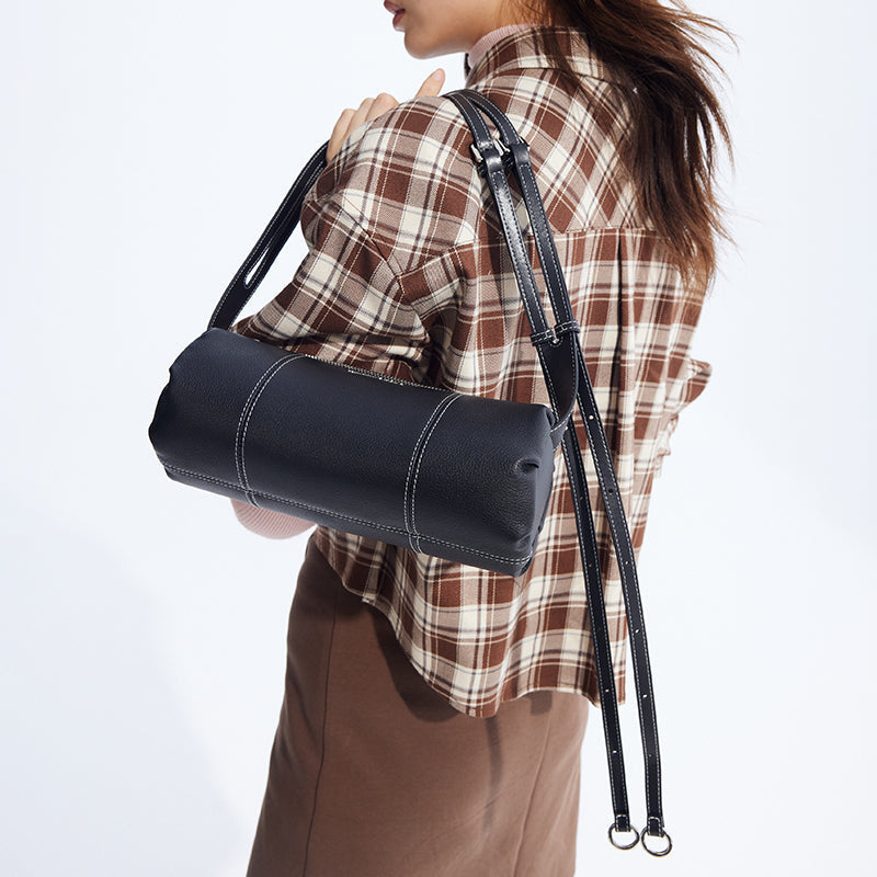 Woman in plaid shirt carries black cylinder shoulder bag with white stitching, Amazing Song