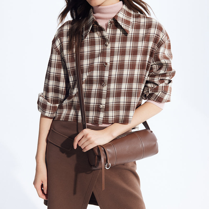 Woman wearing brown plaid shirt and brown skirt, holding a brown leather shoulder bag