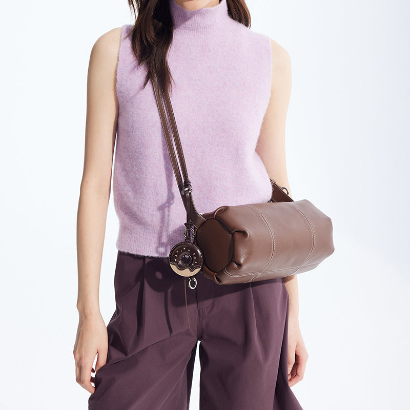 Woman wearing lilac sleeveless sweater, brown crossbody leather bag, and purple pants