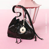 Black Amazing Song bucket bag with donut keychain on pink surface near pink lantern