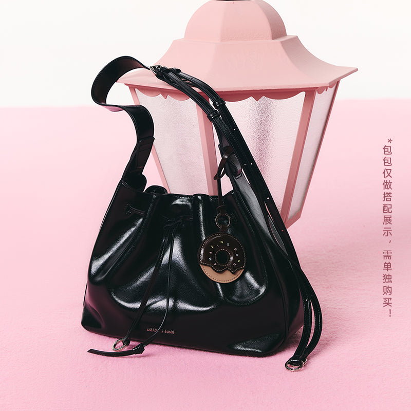 Amazing Song black leather bucket bag with round tag, displayed on pink background beside lantern