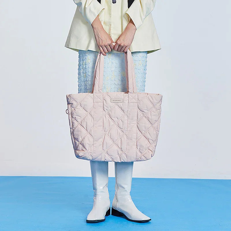 Woman holding a large quilted pastel pink tote bag, white boots, blue skirt, Amazing Song