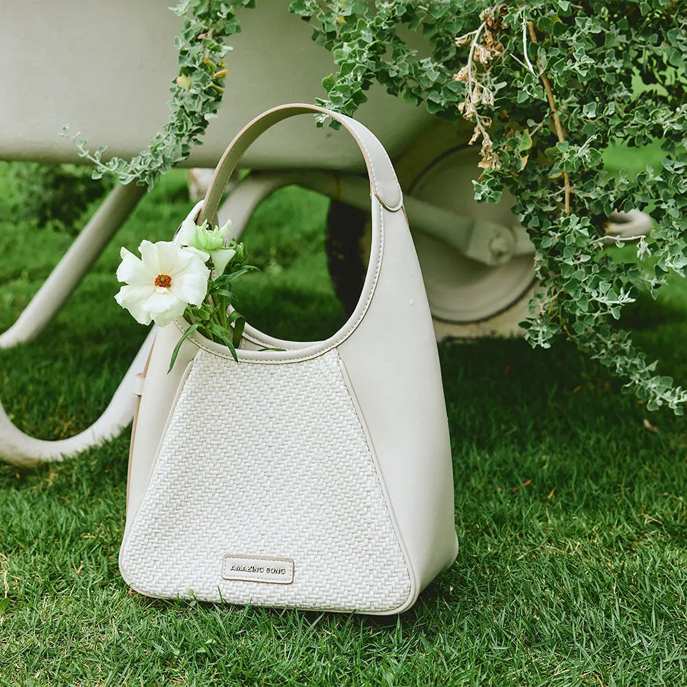 Amazing Song white woven handbag with flower outdoors on grass by vintage cart