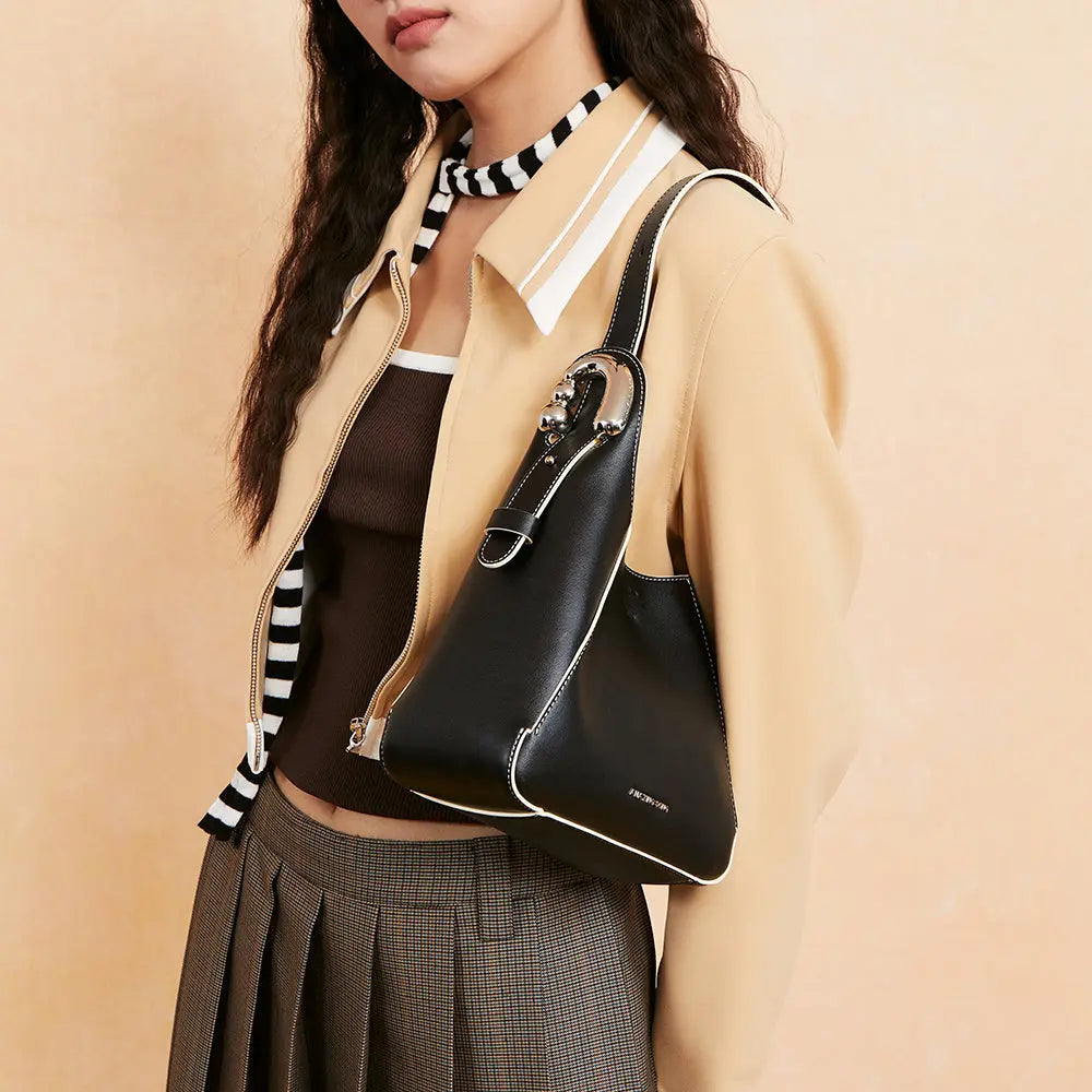 Woman in a beige jacket carrying a black Amazing Song handbag with white trim