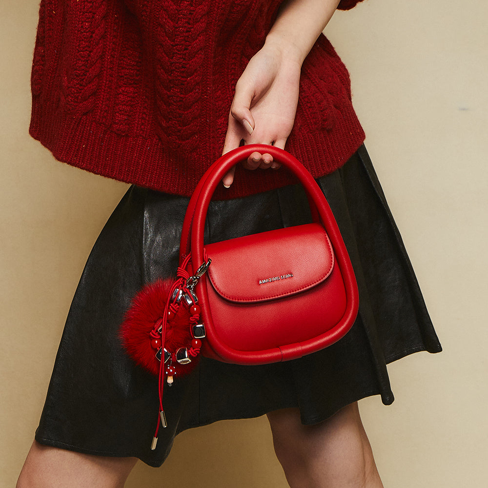 Woman holding red Amazing Song handbag with charm, wearing red sweater and black skirt