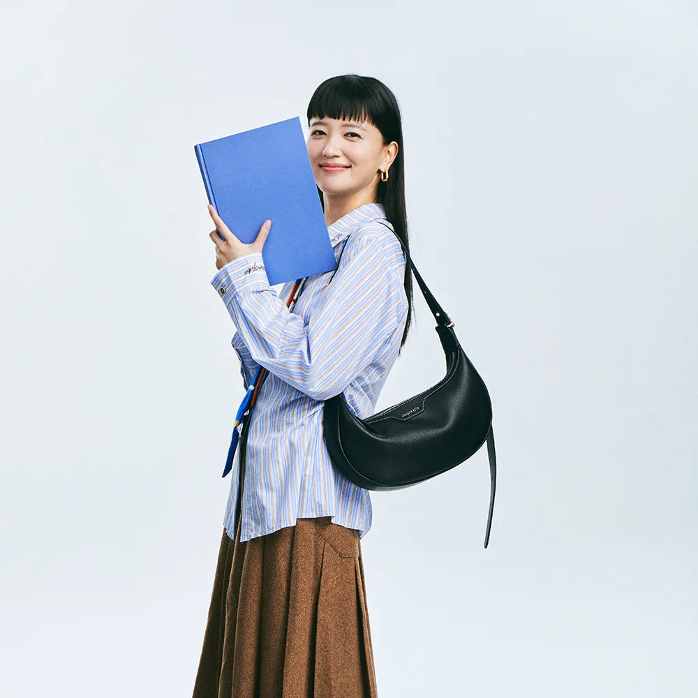 Smiling woman with blue book, striped shirt, brown skirt, and black shoulder bag