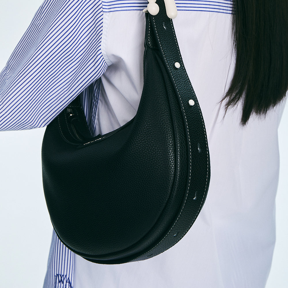 Black leather shoulder bag with white stitching worn over striped shirt, Amazing Song