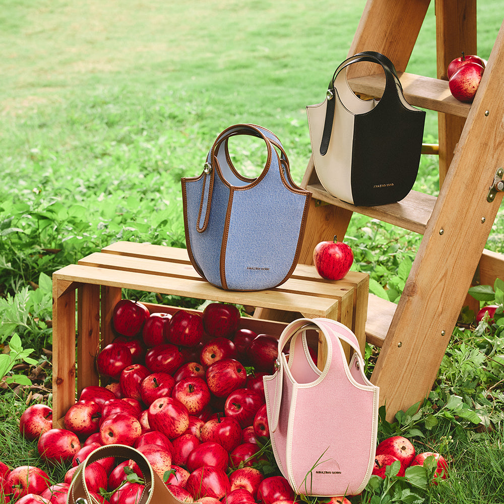 Amazing Song designer handbags in blue, black, and pink displayed outdoors with apples