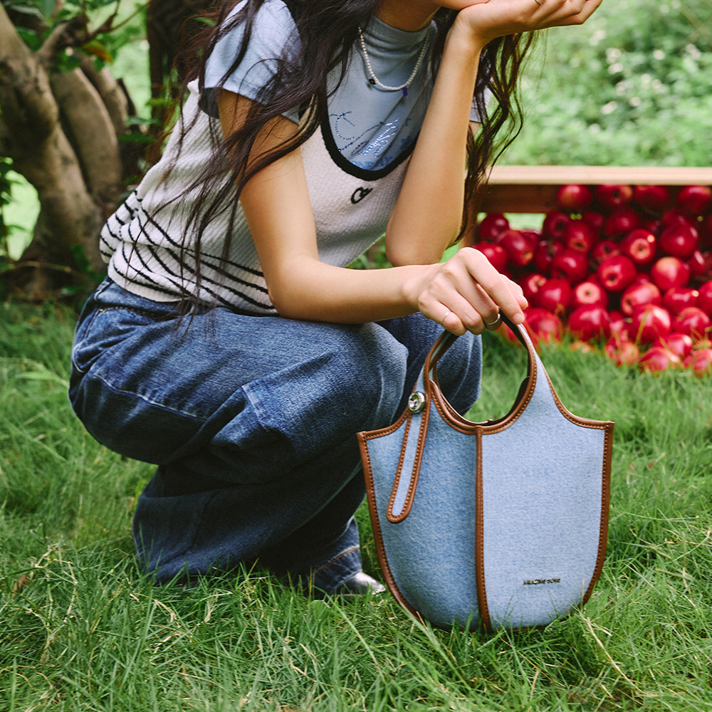 Woman outdoors with denim Amazing Song bag on grass, apples in background