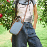 Woman in striped top and jeans with blue Amazing Song crossbody bag outdoors near apple tree