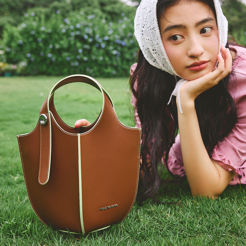 Woman in a bonnet with brown Amazing Song handbag on grass, outdoor fashion photo