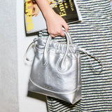 Close-up of a person holding a silver Amazing Song handbag and a fashion magazine