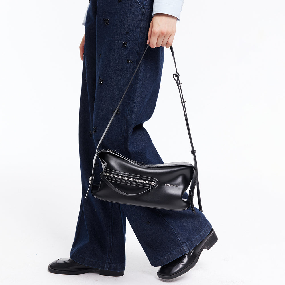 Person in wide-leg jeans holding Amazing Song black leather shoulder bag with zipper